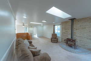 Living room with a skylight, a wood stove, ornamental molding, and brick wall