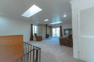 Carpeted living room featuring a wood stove, crown molding, and a skylight