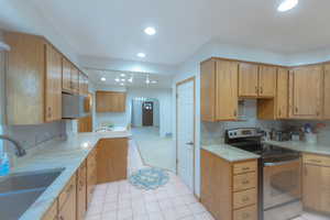 Kitchen with light stone countertops, sink, rail lighting, electric stove, and light tile patterned floors