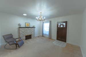 Carpeted foyer featuring a stone fireplace, crown molding, and a chandelier