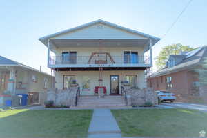 View of front facade with a front yard, a balcony, and covered porch