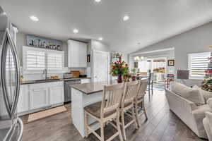 Kitchen with sink, vaulted ceiling, appliances with stainless steel finishes, decorative light fixtures, and white cabinetry