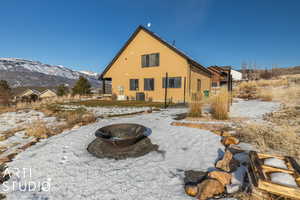 Snow covered back of property with a mountain view, a fire pit, and central air condition unit