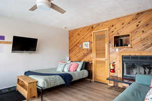 Bedroom with ceiling fan, wood-type flooring, and wooden walls