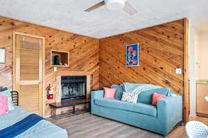 Living room with hardwood / wood-style floors, a textured ceiling, ceiling fan, and wood walls