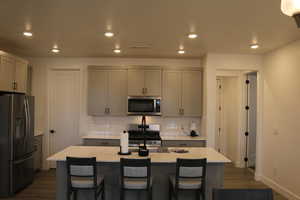 Kitchen featuring appliances with stainless steel finishes, backsplash, dark hardwood / wood-style flooring, gray cabinets, and an island with sink