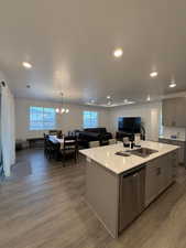 Kitchen with gray cabinetry, a kitchen island with sink, sink, stainless steel dishwasher, and hardwood / wood-style flooring