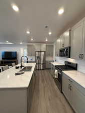 Kitchen with a center island with sink, gray cabinetry, sink, and appliances with stainless steel finishes