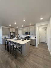 Kitchen with gray cabinetry, sink, dark hardwood / wood-style flooring, a kitchen island with sink, and appliances with stainless steel finishes