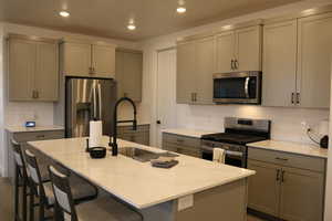 Kitchen featuring gray cabinets, a center island with sink, and appliances with stainless steel finishes