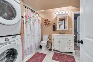 Full bathroom featuring shower / bath combo with shower curtain, vanity, stacked washing maching and dryer, and toilet