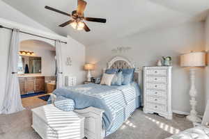 Carpeted bedroom with ensuite bath, ceiling fan, and lofted ceiling