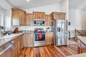 Kitchen featuring dark hardwood / wood-style flooring, stainless steel appliances, vaulted ceiling, and sink