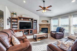 Living room with a textured ceiling, a stone fireplace, ceiling fan, and lofted ceiling