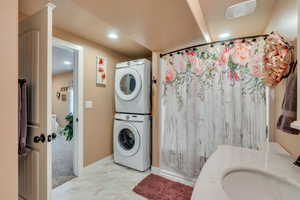 Washroom with a textured ceiling, sink, and stacked washer / dryer