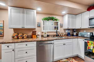 Kitchen featuring appliances with stainless steel finishes, dark stone counters, sink, hardwood / wood-style flooring, and white cabinets