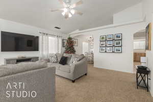 Carpeted living room featuring ceiling fan with notable chandelier and vaulted ceiling