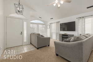 Carpeted living room with ceiling fan with notable chandelier, vaulted ceiling, and a wealth of natural light