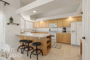 Kitchen with light brown cabinets, white appliances, a kitchen breakfast bar, sink, and kitchen peninsula