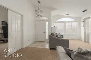 Foyer entrance featuring a notable chandelier, light colored carpet, and vaulted ceiling