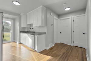 Kitchen featuring stainless steel dishwasher, dark hardwood / wood-style floors, white cabinets, and sink