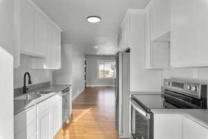 Kitchen with white cabinets, stainless steel appliances, light hardwood / wood-style flooring, and sink