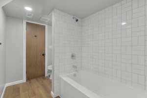 Basement bathroom featuring hardwood / wood-style flooring, tiled shower / bath combo, and toilet