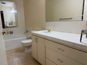 Bathroom with backsplash, a tub, vanity, and toilet. In the hallway.