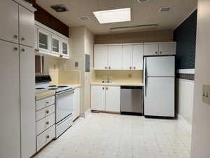 Kitchen with white cabinets, white appliances, and a skylight