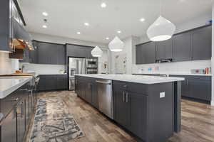 Kitchen featuring dark hardwood / wood-style flooring, pendant lighting, decorative backsplash, a center island with sink, and appliances with stainless steel finishes