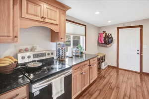 Kitchen with dark stone countertops, electric range, light brown cabinets, and light hardwood / wood-style floors