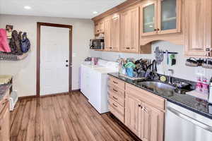 Kitchen featuring stainless steel dishwasher, washer and clothes dryer, light brown cabinetry, and hardwood / wood-style flooring