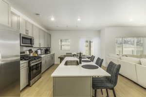 Kitchen featuring appliances with stainless steel finishes, sink, light hardwood / wood-style flooring, gray cabinets, and an island with sink