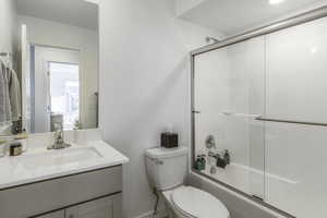 Full bathroom featuring vanity, toilet, and bath / shower combo with glass door