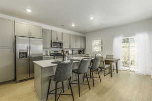 Kitchen featuring gray cabinetry, light hardwood / wood-style floors, a kitchen island with sink, and appliances with stainless steel finishes