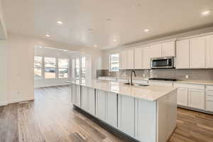 Kitchen featuring an island with sink, backsplash, light wood-type flooring, white cabinets, and sink