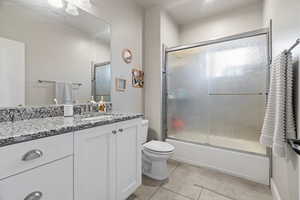 Full bathroom featuring toilet, vanity, tile patterned floors, and bath / shower combo with glass door