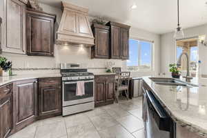 Kitchen with pendant lighting, backsplash, premium range hood, sink, and appliances with stainless steel finishes