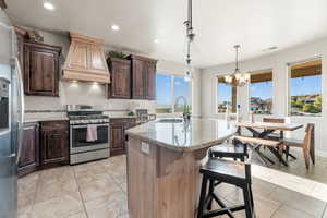 Kitchen featuring appliances with stainless steel finishes, tasteful backsplash, pendant lighting, a center island with sink, and a chandelier