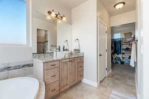 Bathroom featuring a wealth of natural light, tile patterned flooring, vanity, and a relaxing tiled tub