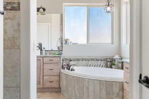 Bathroom featuring a chandelier, vanity, tiled bath, and tile patterned floors