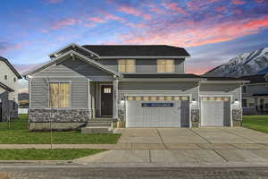 View of front of home with stone siding, a yard, and concrete driveway