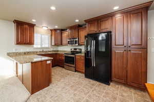 Kitchen featuring kitchen peninsula, light stone counters, sink, and appliances with stainless steel finishes