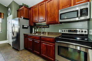 Kitchen with light tile patterned flooring, appliances with stainless steel finishes, dark stone countertops, and sink