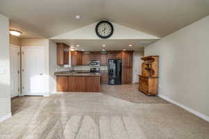 Kitchen with light colored carpet, kitchen peninsula, stainless steel appliances, and vaulted ceiling