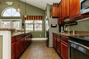 Kitchen with dark stone counters, sink, stainless steel appliances, and dark tile patterned flooring