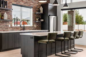 Bar featuring stainless steel fridge, brick wall, sink, light hardwood / wood-style floors, and hanging light fixtures