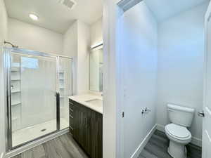 Bathroom with hardwood / wood-style floors, vanity, toilet, and a shower with shower door