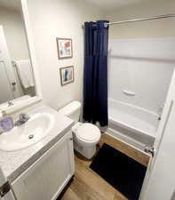 Full bathroom with toilet, vanity, shower / bath combination with curtain, and hardwood / wood-style flooring