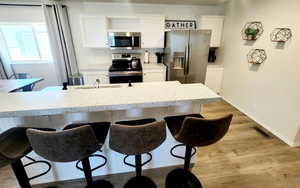 Kitchen with white cabinets, appliances with stainless steel finishes, a breakfast bar, and light wood-type flooring